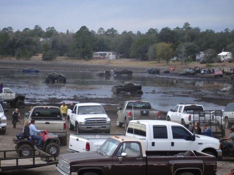 1989 Ford Bronco - Multiple trucks and ATVs are stuck in the mud at an outdoor event.