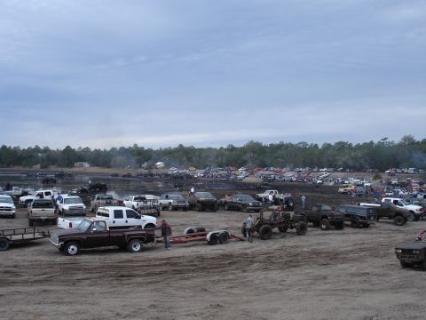 1989 Ford Bronco - A large gathering of trucks and people are present at an outdoor event, possibly a mud bog or off-road park.