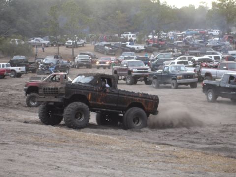 1989 Ford Bronco - A heavily modified pickup truck navigates a muddy terrain, surrounded by numerous other vehicles.