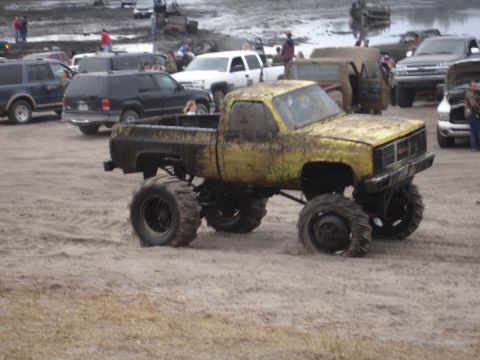 1989 Ford Bronco - A heavily modified yellow pickup truck navigates a muddy terrain with other vehicles in the background.