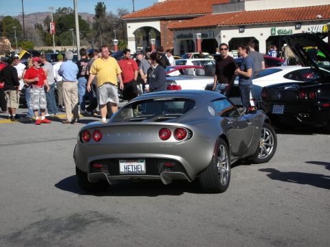 1998 Ford Crown Victoria - silver Lotus Elise with a HETHEL vanity plate parks among a crowd of spectators at an outdoor car show.