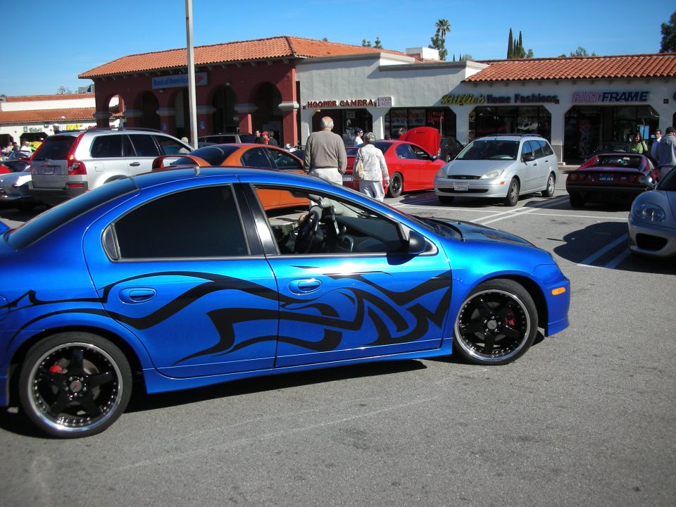 Blue Dodge Neon with black tribal graphics and black wheels at a car show