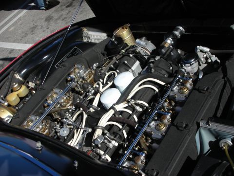 1998 Ford Crown Victoria - meticulously detailed V12 engine with chrome and braided lines fills the engine bay of a classic sports car at a show.