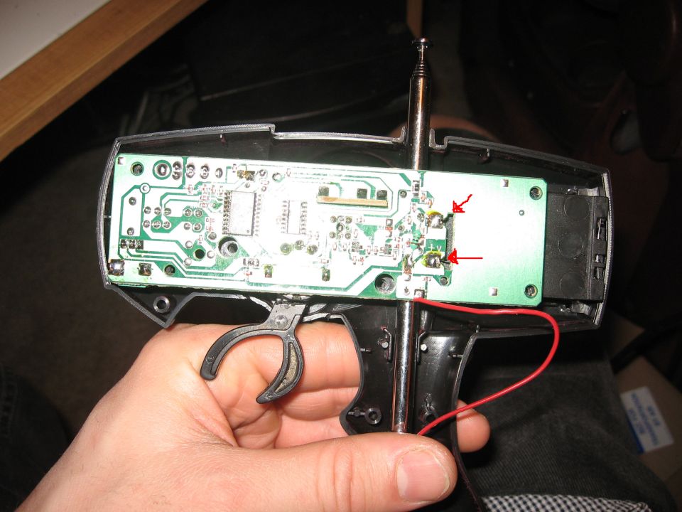 Remote control circuit board with red arrows pointing to solder points, held in a hand