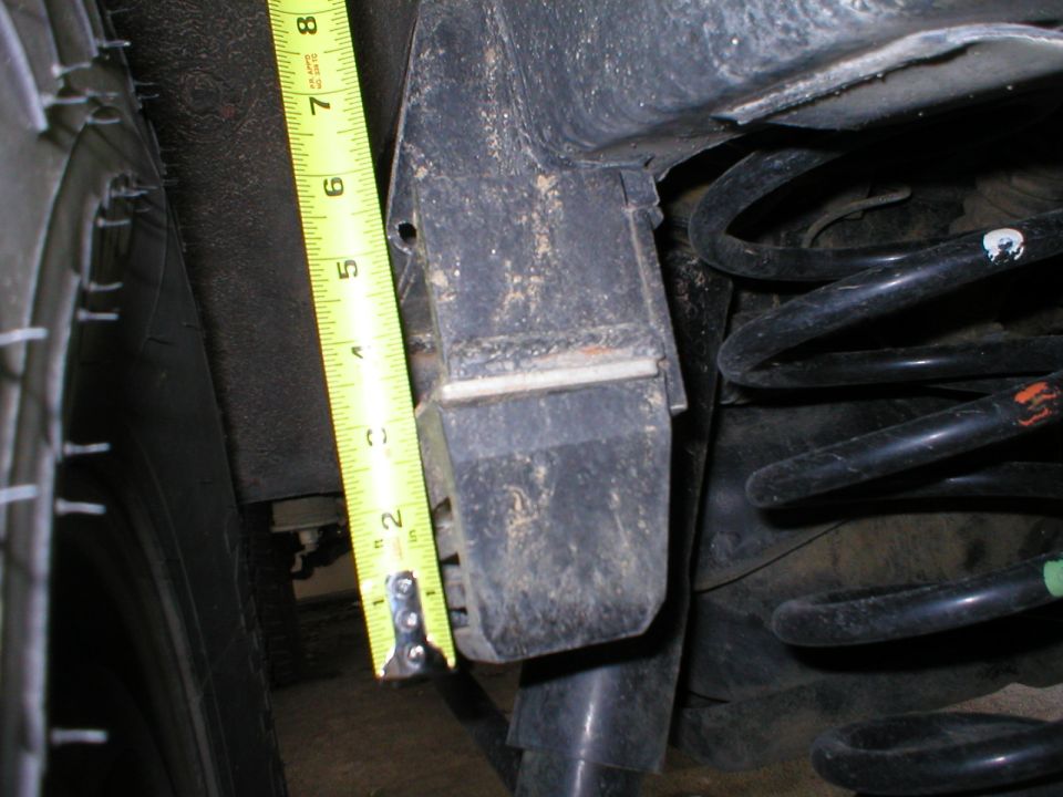 Tape measure next to a vehicle's rear coil spring and suspension component