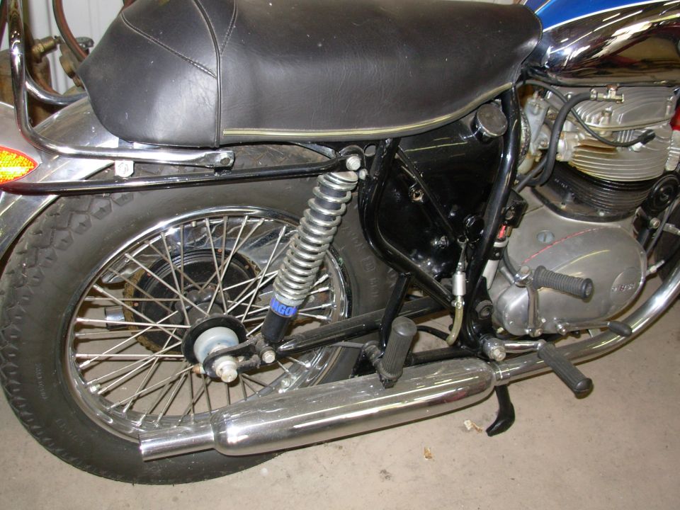Rear right side of classic motorcycle with spoked wheel, shock, chrome exhaust and finned engine