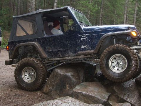 1991 Jeep Wrangler - A 1991 Jeep Wrangler is shown off-road, climbing over large rocks with its tires.