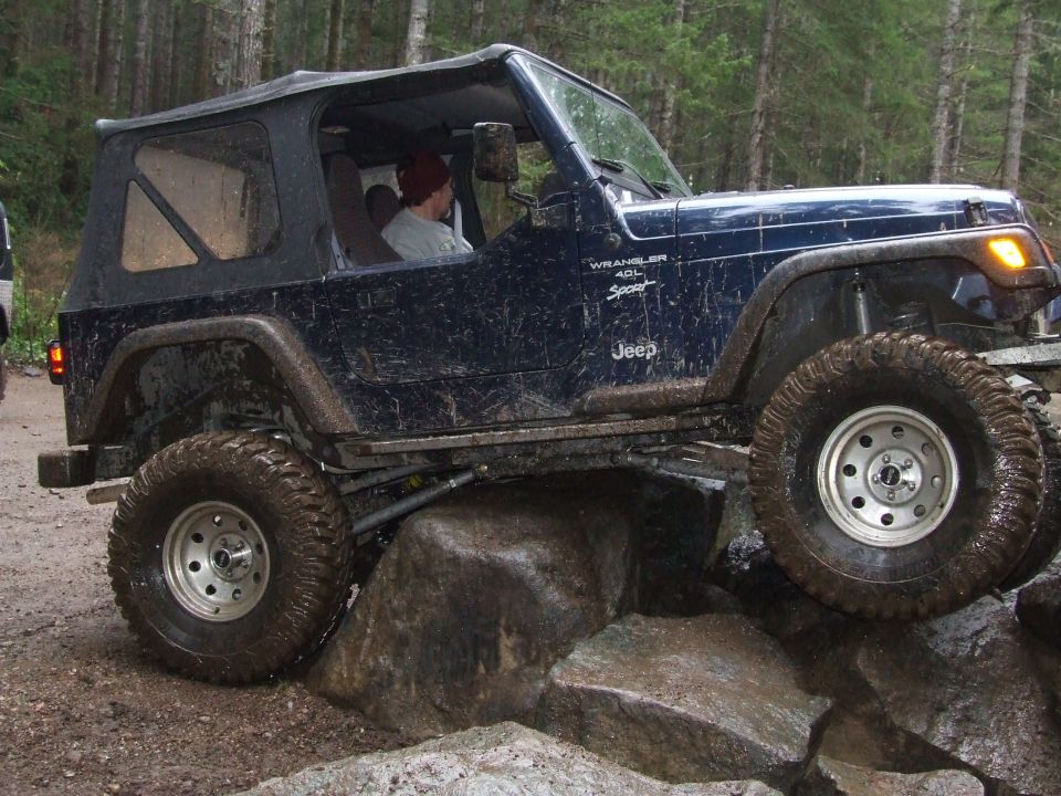 Dark blue 1991 Jeep Wrangler with a black soft top navigating large rocks on a dirt trail