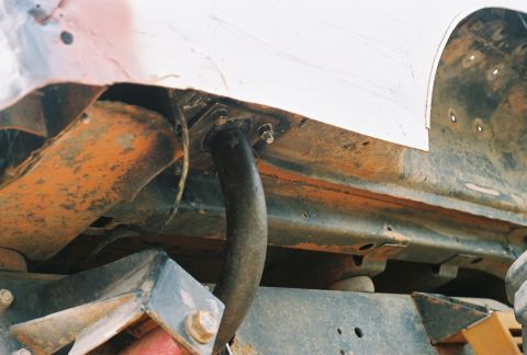 1978 Ford Bronco - Low-angle film photo of a truck's rusted rocker and frame seam with a black bent steel tube bolted through a bracket into the frame rail, p…
