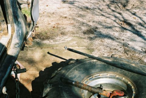 1978 Ford Bronco - A close-up view of a large off-road tire with a chrome multi-lug wheel, with a long steel pry bar or breaker bar resting across it, photogr…