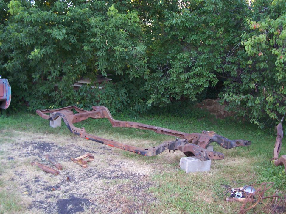 rusted vehicle frame sitting on grass, supported by concrete blocks