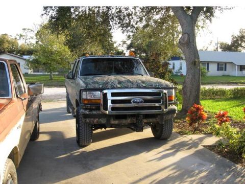 1974 Ford F-100 - A camo-wrapped Ford F-Series truck is parked in a driveway next to another truck.