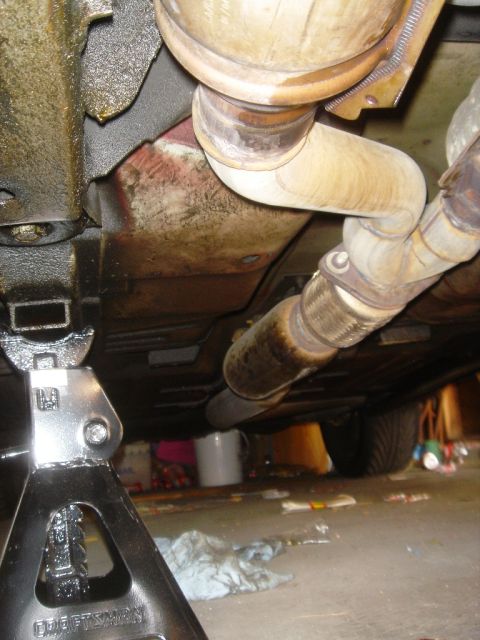 1991 Ford Taurus - Underside view of a vehicle's exhaust system, held up by a jack stand.