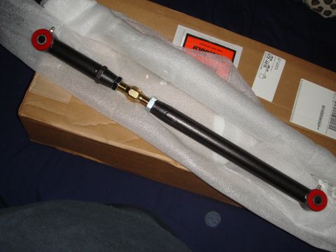 1993 Ford Taurus - An adjustable suspension control arm with red bushings and a brass fitting is shown, likely a replacement part for a vehicle.