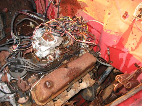 1952 Ford Pickup - The engine bay of a vehicle shows a rusty V8 engine with a tangled mess of wires and a carburetor.