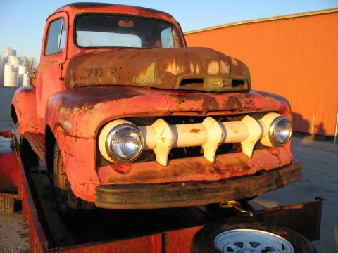 1952 Ford Pickup - A weathered 1952 Ford Pickup truck, showing significant rust, is positioned on a trailer against an orange building.