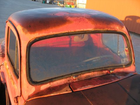 1952 Ford Pickup - Close-up of a weathered 1952 Ford Pickup truck cab, showing rust and a damaged windshield.