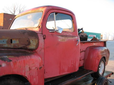 1952 Ford Pickup - A heavily rusted red pickup truck is viewed from the side, resting on a trailer.