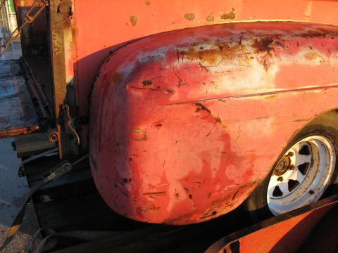1952 Ford Pickup - Close-up of a weathered 1952 Ford Pickup's red fender and wheel, showing signs of age and damage.