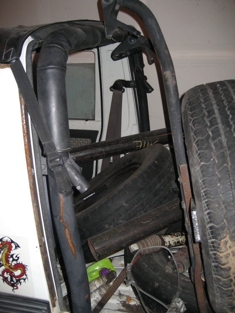 Padded roll bar and worn seat inside stripped white 4x4 with spare tire alongside