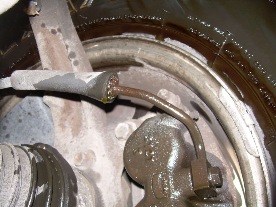 close-up of a greasy brake caliper and fluid line with a portion of the tire visible