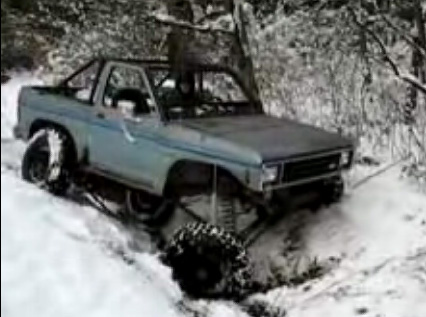 1984 Ford Bronco II - An off-road SUV navigates a snowy trail, its large tires digging into the snow. The Supermotors.net logo is visible in the lower right corn…