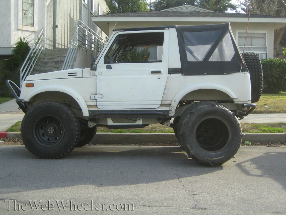 White Suzuki Samurai with large off-road tires and a soft top parked on a street