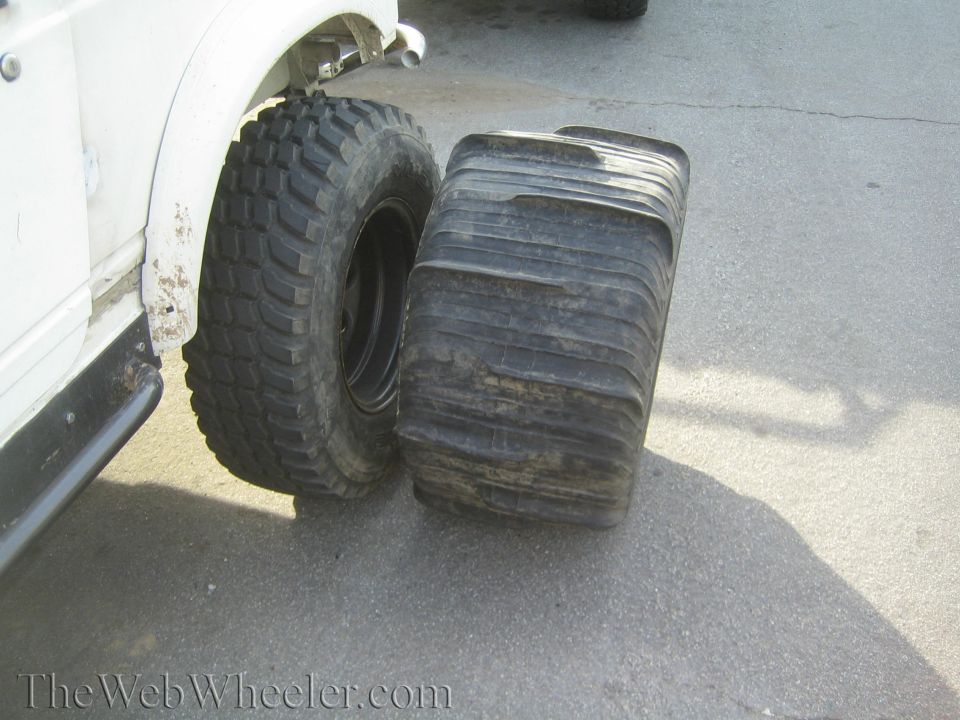 White off-road truck beside a large worn flotation tire compared to mounted mud tire