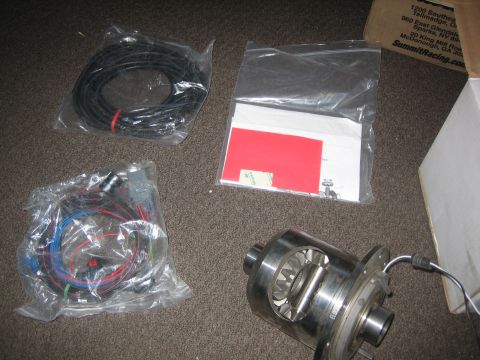 1995 Ford Bronco - Parts for a vehicle differential rebuild are laid out on the floor, including wiring harnesses and the differential itself.