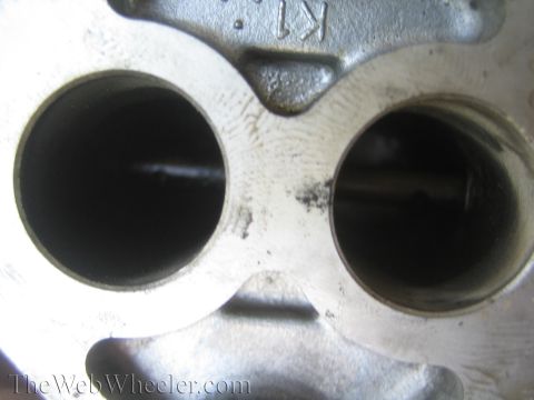 1990 Ford Bronco - Macro view of two round bores in a cast-metal engine part, each showing a thin slot across the opening.