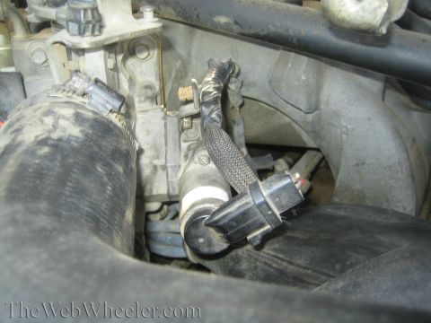 1990 Ford Bronco - electrical connector and braided metal hose routed through a dusty engine bay near a black intake tube.