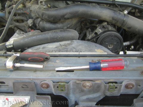 1990 Ford Bronco - Two screwdrivers, one red and one with a clear handle, rest across a radiator support in an open engine bay.