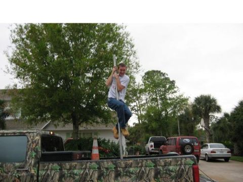 1974 Ford F-100 - A person climbs a pole extending from the bed of a camouflage truck, with other vehicles parked nearby.