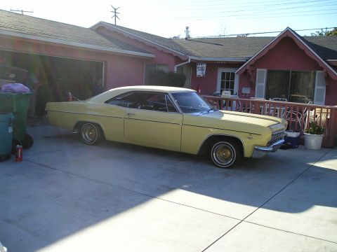 1986 Ford Bronco II - A yellow 1965 coupe is parked in a driveway in front of a house.