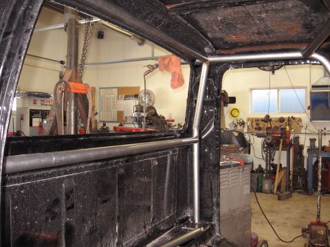 1977 Ford F-150 - The interior of a truck is shown with a roll cage, set against a backdrop of a workshop environment.
