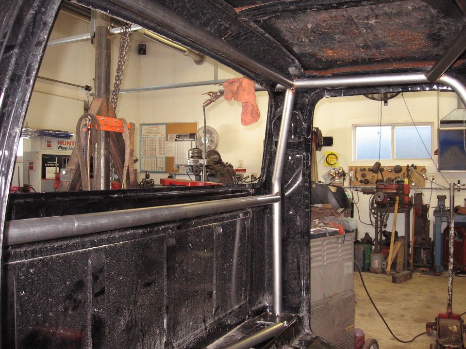 Inside of a truck cab with a roll cage installed, looking towards a workshop with tools and machinery