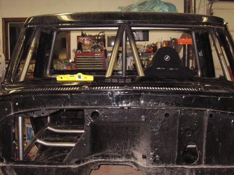 1977 Ford F-150 - The interior of a truck cab shows a custom roll cage and a racing seat, with tools in the background.
