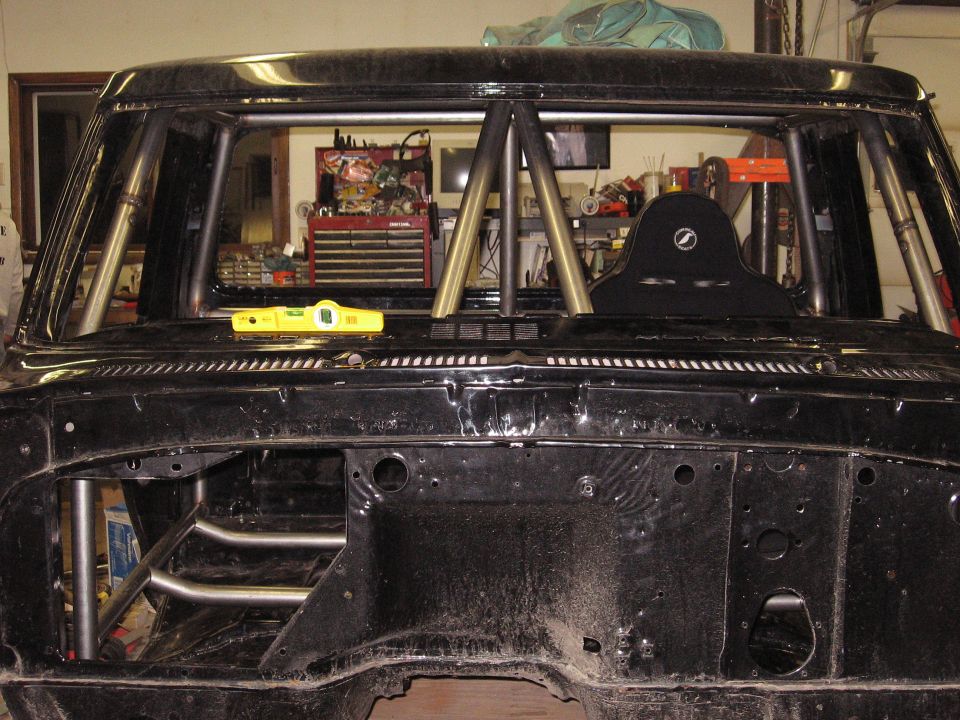 Truck cab with roll cage installed, racing seat visible. Toolbox and equipment in background