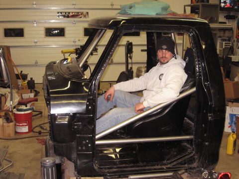 1977 Ford F-150 - Man sits inside the modified cab of a 1977 Ford F-150, which has a roll cage installed.