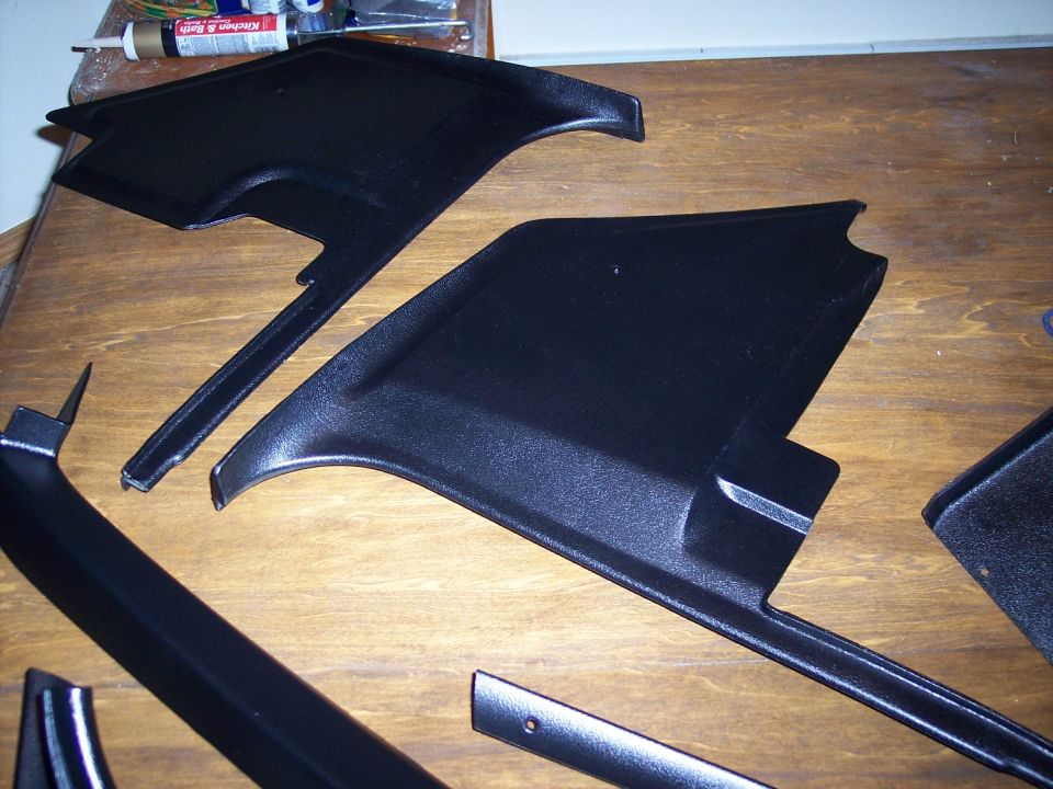 Several black plastic interior trim pieces laid out on a wooden surface