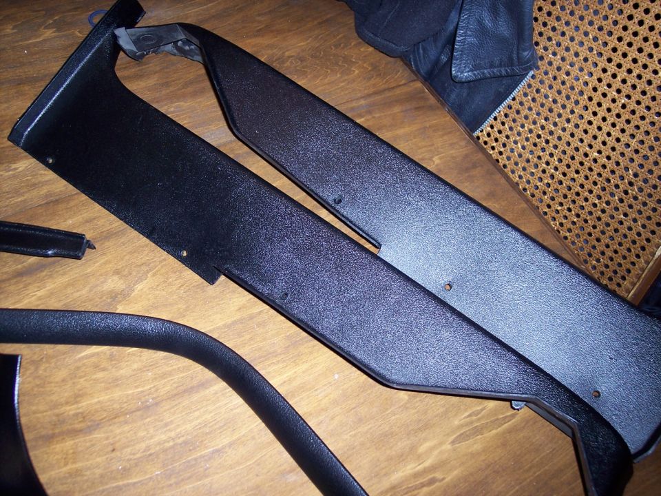 Refinished black interior trim panels and molding laid out on a hardwood floor