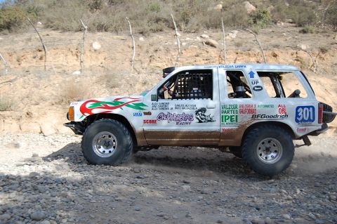 1992 Ford Explorer - A white off-road SUV with racing decals drives on a dirt road, kicking up dust.