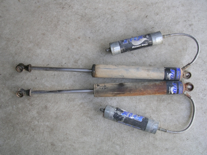Two pairs of Fox Racing Shox shock absorbers, one pair is dirty and rusty, the other is cleaner
