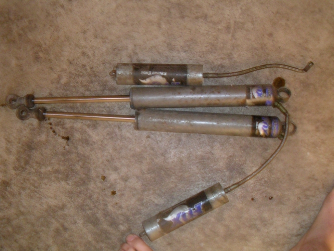 Four used shock absorbers with copper shafts and silver bodies, some with blue and white decals