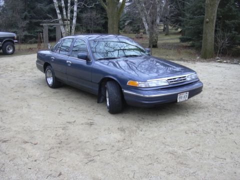 1996 Ford Crown Victoria - A blue Ford Crown Victoria is parked outside next to a pickup truck.