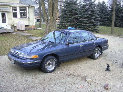 1996 Ford Crown Victoria - A blue Ford Crown Victoria is parked in a gravel driveway next to a house.