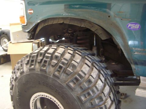 1996 Ford Bronco - A close-up view of the fender and wheel well of a green 1996 Ford Bronco, showing a large off-road tire and a Harley-Davidson emblem.