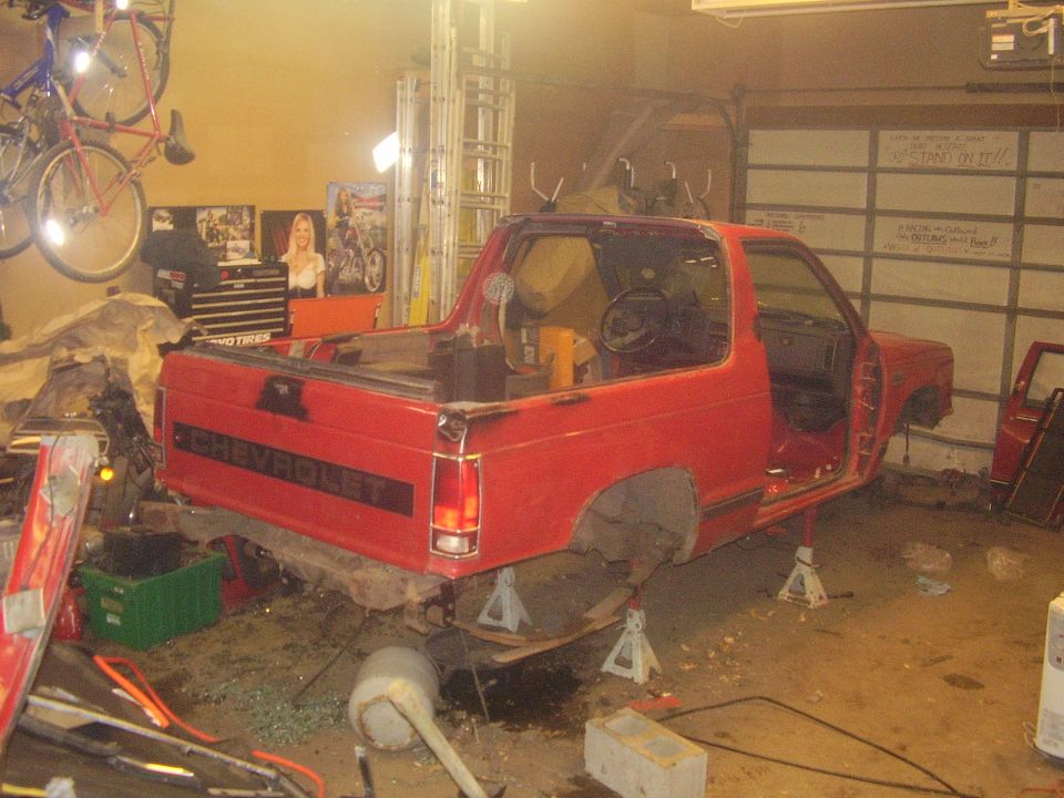 Red 1990 Chevrolet pickup truck on jack stands in garage, doors removed