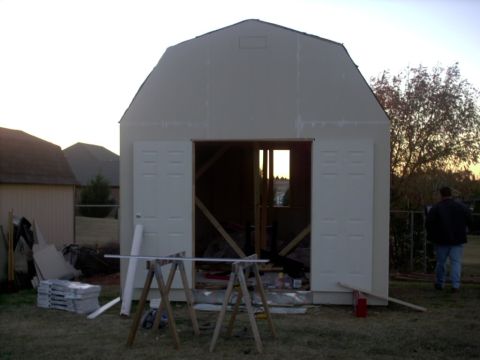 1965 Ford Mustang - An unfinished shed with construction materials in the yard, a person walks away from the structure.