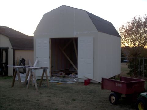 1965 Ford Mustang - A shed is being built, with its doors open and construction materials visible inside and around the structure.